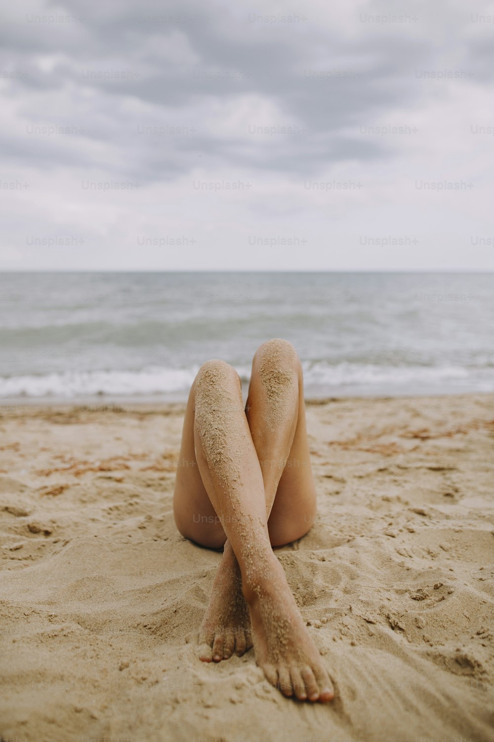 Gambe abbronzate femminili con sabbia su pelle liscia primo piano sulla spiaggia. Bella immagine autentica e creativa. Giovane donna che si rilassa in riva al mare. Vacanze estive. Cura dei piedi