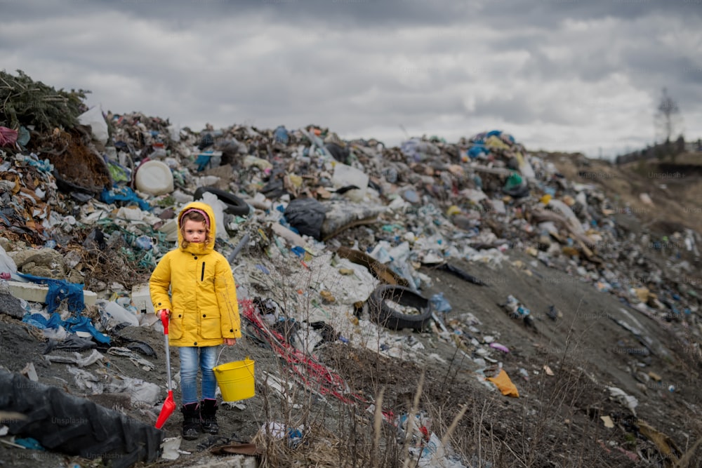 Front view of small child standing on landfill, environmental pollution concept. Copy space.