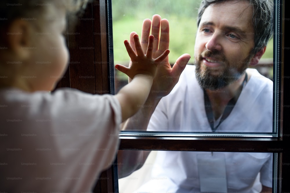 Arzt kommt, um Familie in Isolation zu sehen und zu begrüßen, Fensterglas trennt sie.