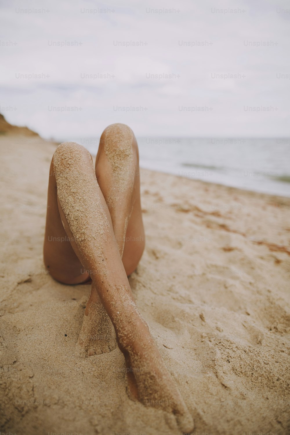 Pernas bronzeadas femininas com areia no closeup da pele lisa na praia. Bela imagem autêntica e criativa. Mulher nova relaxando à beira-mar. Férias de verão. Cuidados com os pés
