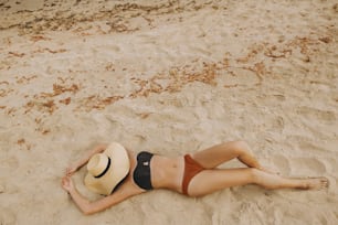 Modische junge Frau mit Strohhut entspannt sich am Sandstrand in der Nähe des Meeres. Sommerurlaub und Reisen. Mädchen am Strand liegend mit Händchenhut. Sorgenfrei. Draufsicht
