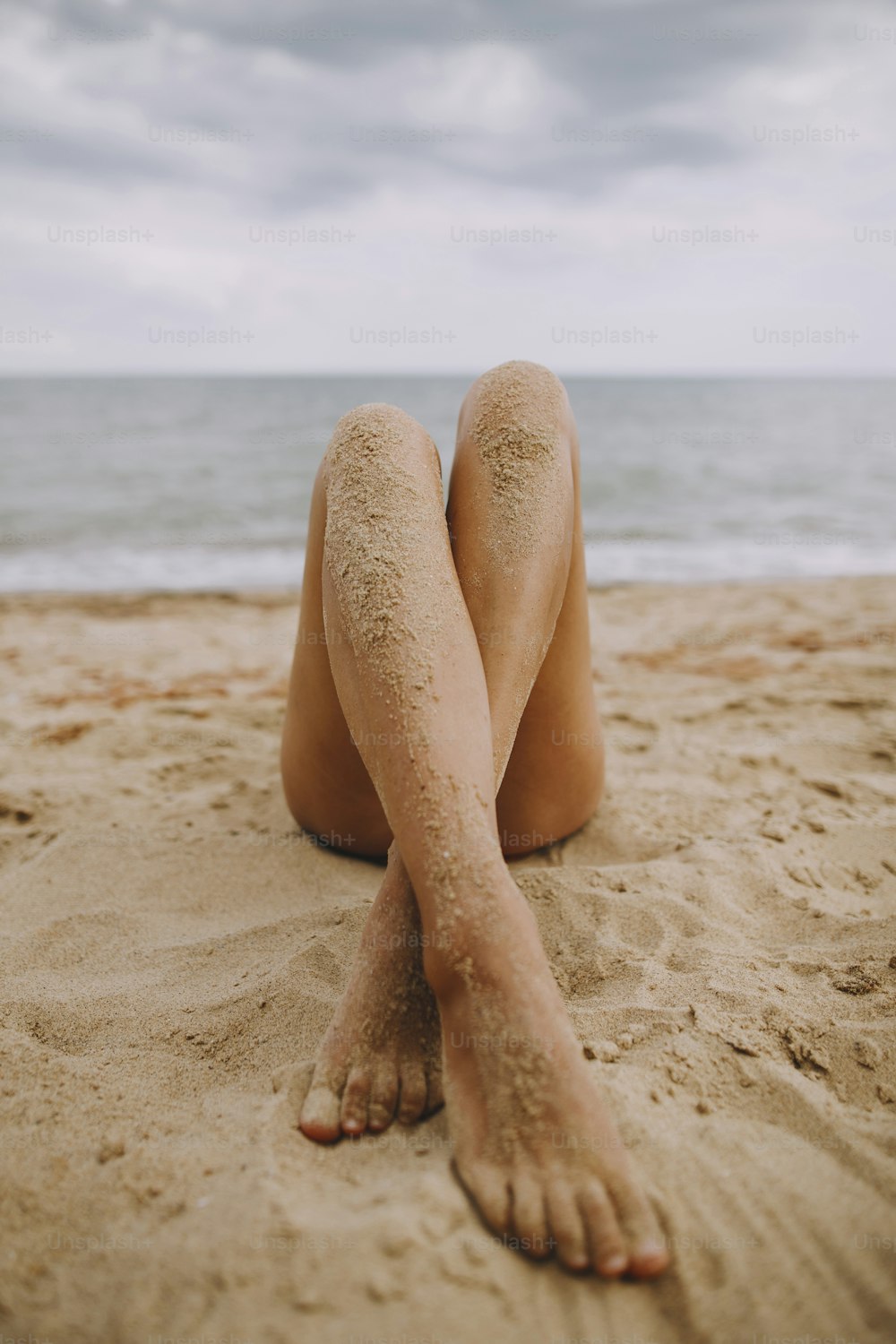 Summer vacation. Tanned legs of a girl on beach with sand on smooth skin. Beautiful authentic and unusual image. Young woman relaxing on seashore.