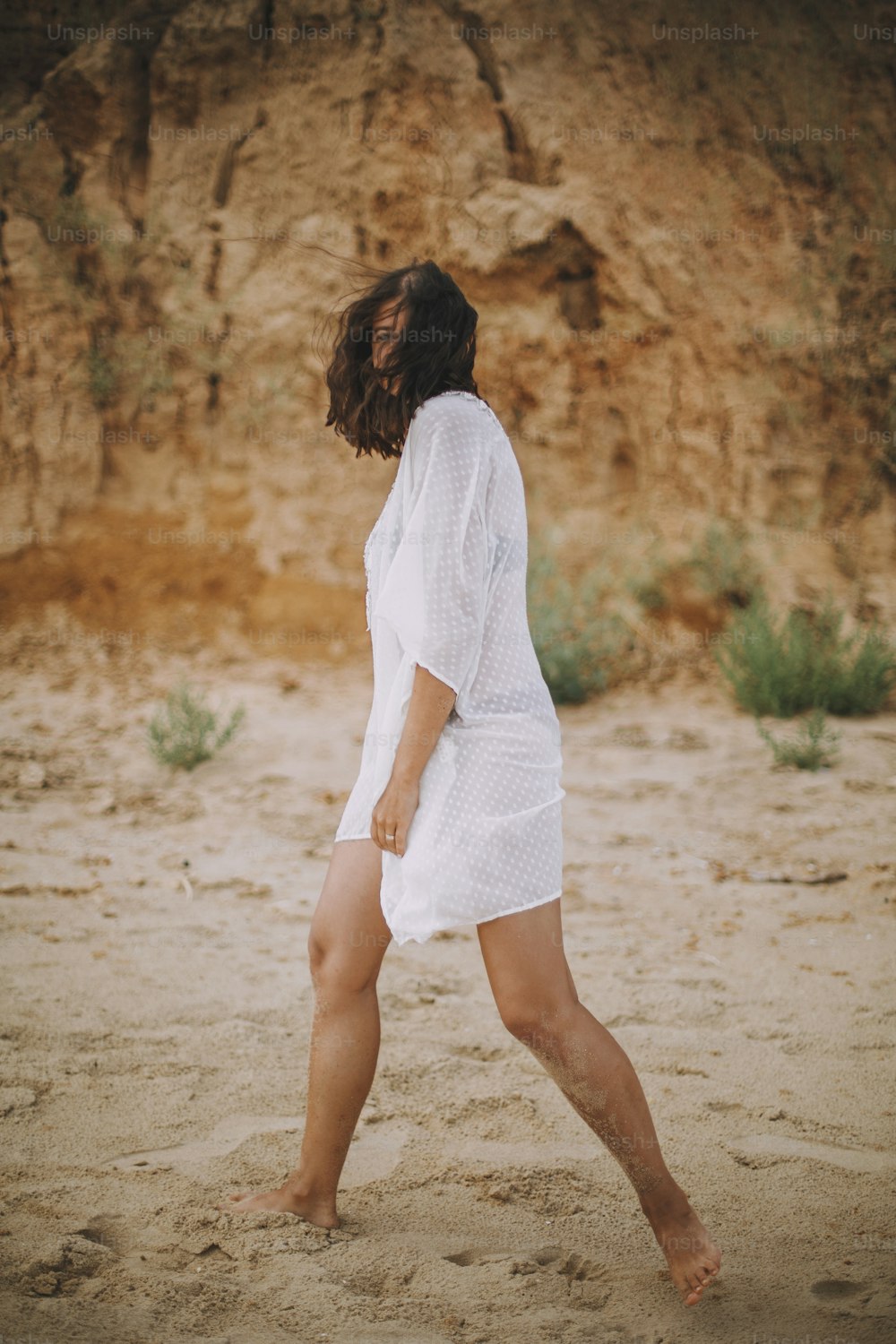 하얀 여름 드레스를 입은 즐거운 보헤미안 소녀가 해변을 걷고 있다. 해변에서 휴식을 취하는 평온한 젊은 여성. 여름 방학. 마음 챙김과 휴식. 생활방식