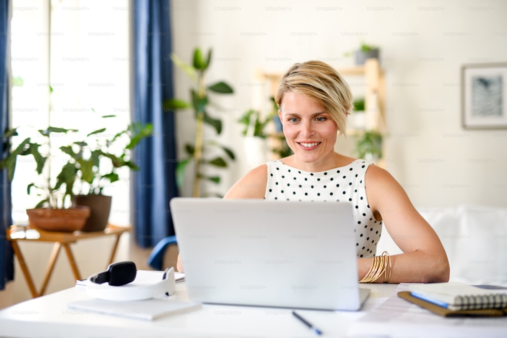 Front view of cheerful young businesswoman with laptop indoors in home office, working.