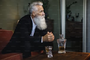 ウイスキーを飲むスタイリッシュでハンサムな髭を生やした老人