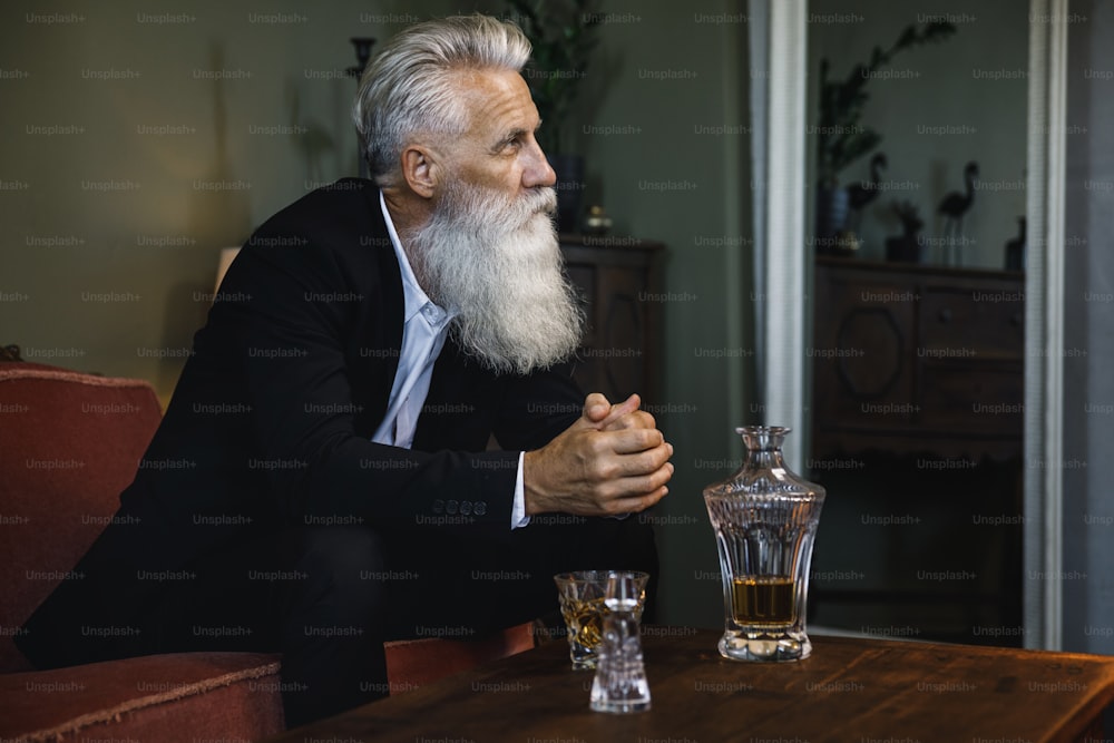 Stilvoller und gutaussehender bärtiger älterer Mann, der Whiskey trinkt