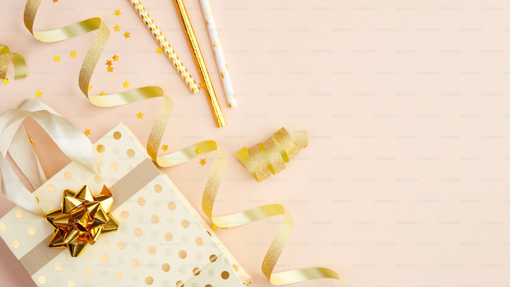 Shopping bag with presents, party streamers and gold confetti stars on beige table. Birthday, Christmas or anniversary celebration concept. Flat lay, top view.
