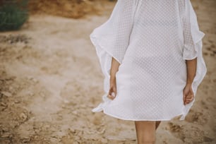 Carefree boho girl in white summer dress walking on beach, back view. Young woman in motion, relax on seashore. Summer vacation. Mindfulness and relaxation. Lifestyle