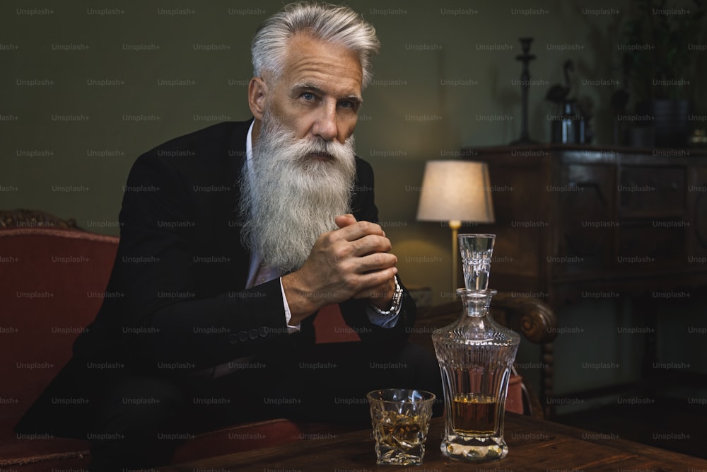 Stilvoller und gutaussehender bärtiger älterer Mann, der Whiskey trinkt