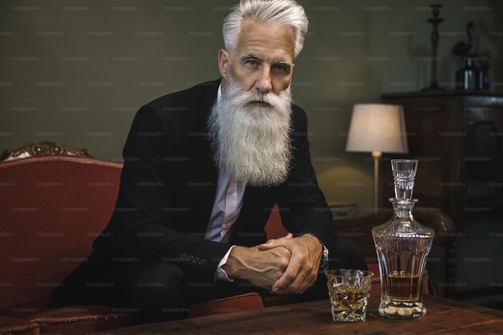 Uomo anziano barbuto elegante e bello che beve whisky