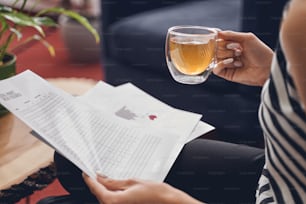 Cropped photo of a woman holding a cup of tea and documents in her hands