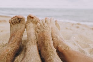 Couple legs in sand close up on sunny beach. Couple in love relaxing together on sandy seashore. Family summer vacation or honeymoon precious moments. Authentic image