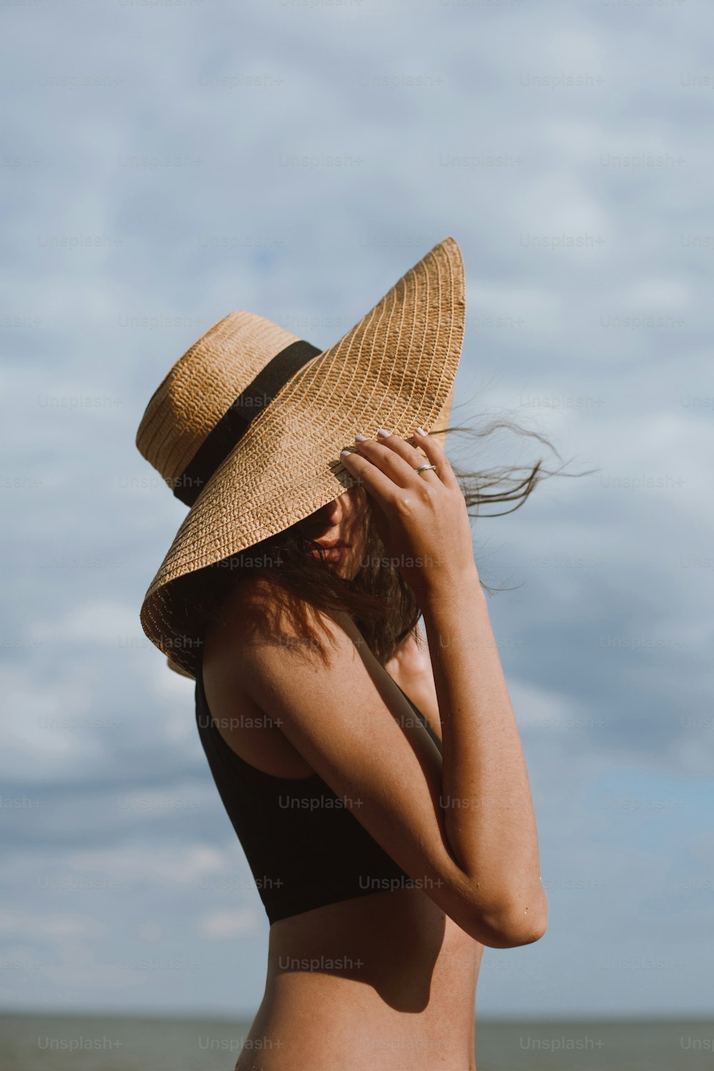 Sensual carefree girl holding hat and posing on background of blue sky in hot summer day. Fashionable tanned woman in straw hat relaxing on beach. Summer vacation