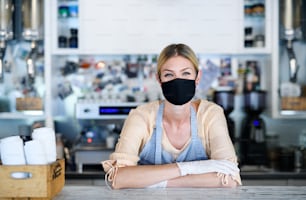 コーヒーショップでフェイスマスクをした女性オーナー、ロックダウン、検疫、コロナウイルス、通常のコンセプトに戻る。
