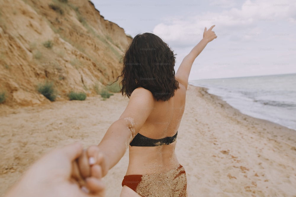 Follow me. Woman leading her man, holding hands on beach. Couple in love on summer vacation or honeymoon. Young woman with sandy tanned body holding man hand