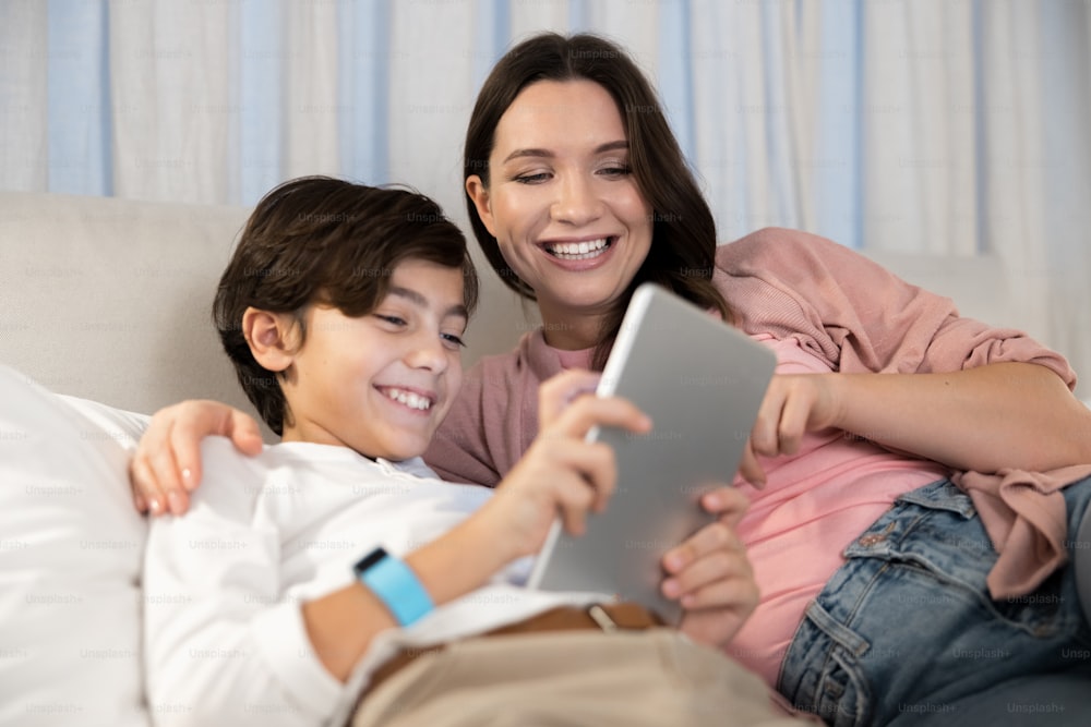 Happy cute short-haired Caucasian boy and a joyous attractive female staring at the tablet screen
