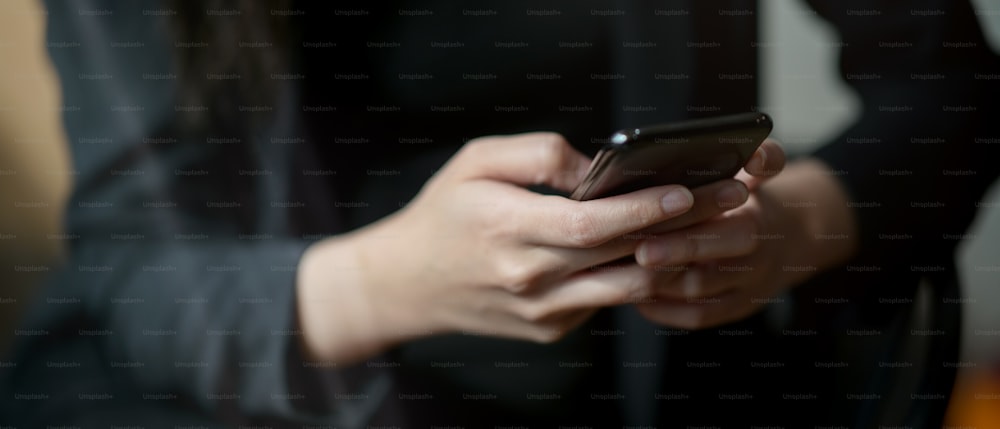 Vista de perto do empresário enviando mensagens de texto no smartphone enquanto está sentado na sala do escritório