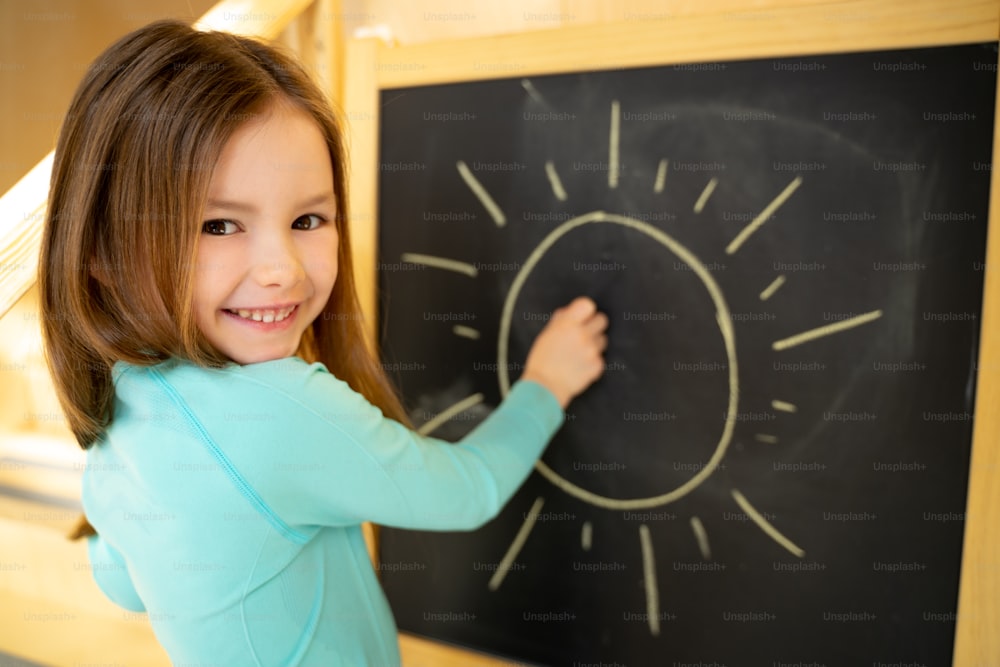 Adorable child drawing on blackboard and smiling stock photo
