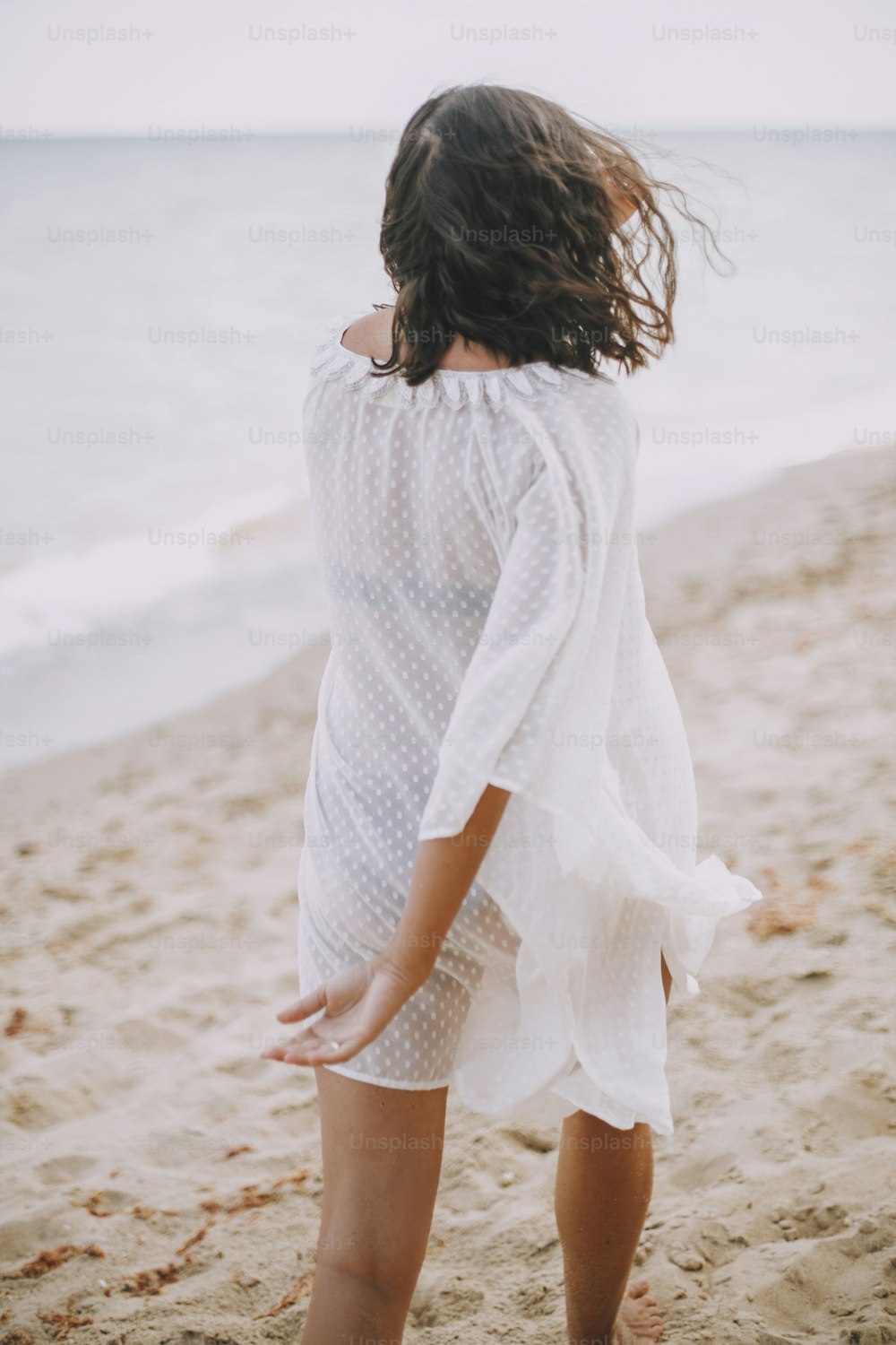 Carefree boho girl in white summer dress walking on beach. Happy young woman relaxing on seashore. Summer vacation. Mindfulness and relaxation. Lifestyle