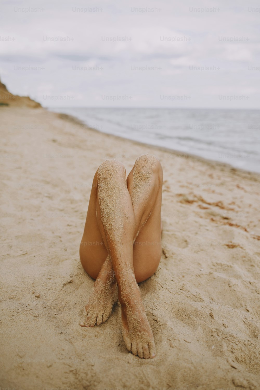 Tanned legs of a girl on beach with sand on smooth skin. Beautiful authentic and unusual image. Young woman relaxing on seashore with sandy legs. Summer vacation. Feet care