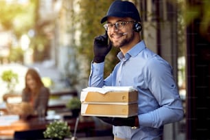 Young happy courier wearing headset while delivering food from a restaurant.
