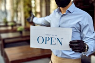 Primer plano del propietario de una cafetería dando la bienvenida a los clientes mientras sostiene un letrero abierto después de la epidemia de COVID-19.