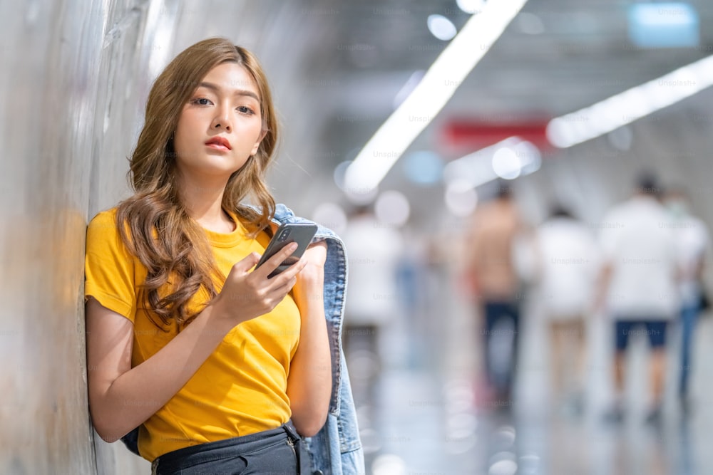 Young beautiful Asian teenage girl using smartphone in subway station.