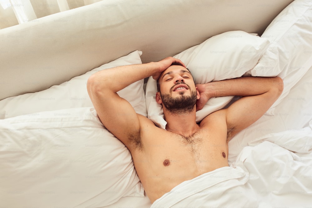 Handsome gentleman resting on white sheets in bedroom and smiling