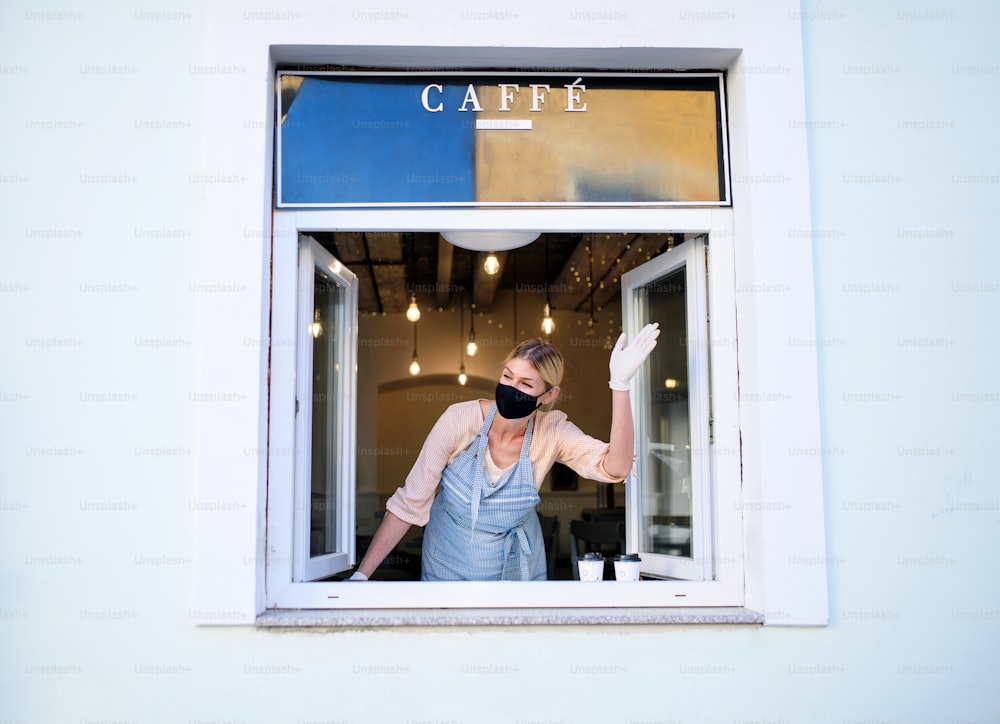 Woman with face mask serving coffee through window, shop open after lockdown quarantine.