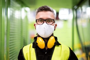 Portrait man worker with protective mask standing in industrial factory or warehouse.