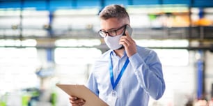 Man technician or engineer with protective mask and telephone working in industrial factory.