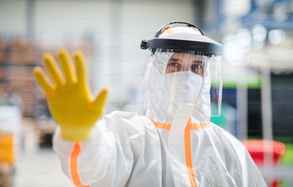 産業工場で保護マスクとスーツを着た労働者の正面図、一時停止標識の手のジェスチャー。