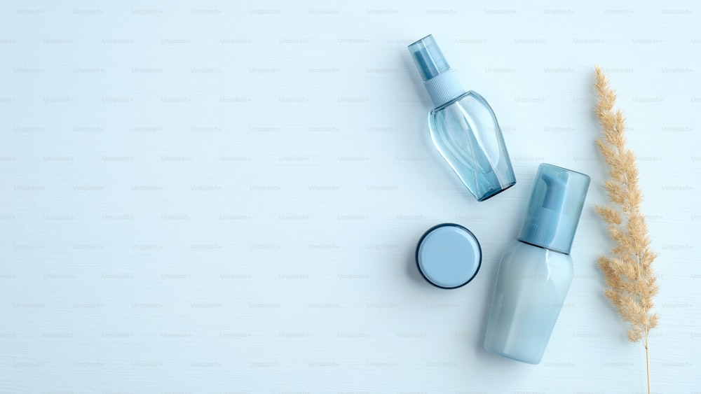 Blaue Kosmetikflaschen und trockene Blume auf blauem Hintergrund. Draufsicht, flach gelegt. Wasserbasierte Schönheitsprodukte Set, minimalistischer Stil.