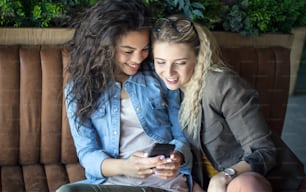 Sharing all. Two smiling girls at cafe using smart phone.