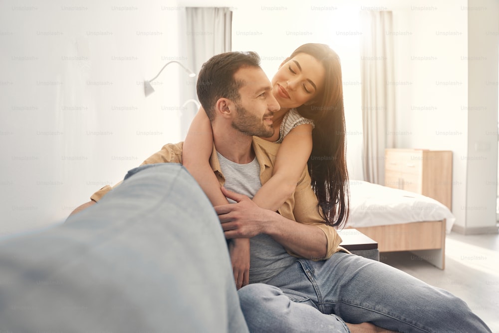 Hombre y mujer sonrientes enamorados que pasan tiempo libre juntos y se sientan en casa en un sofá acogedor, abrazándose