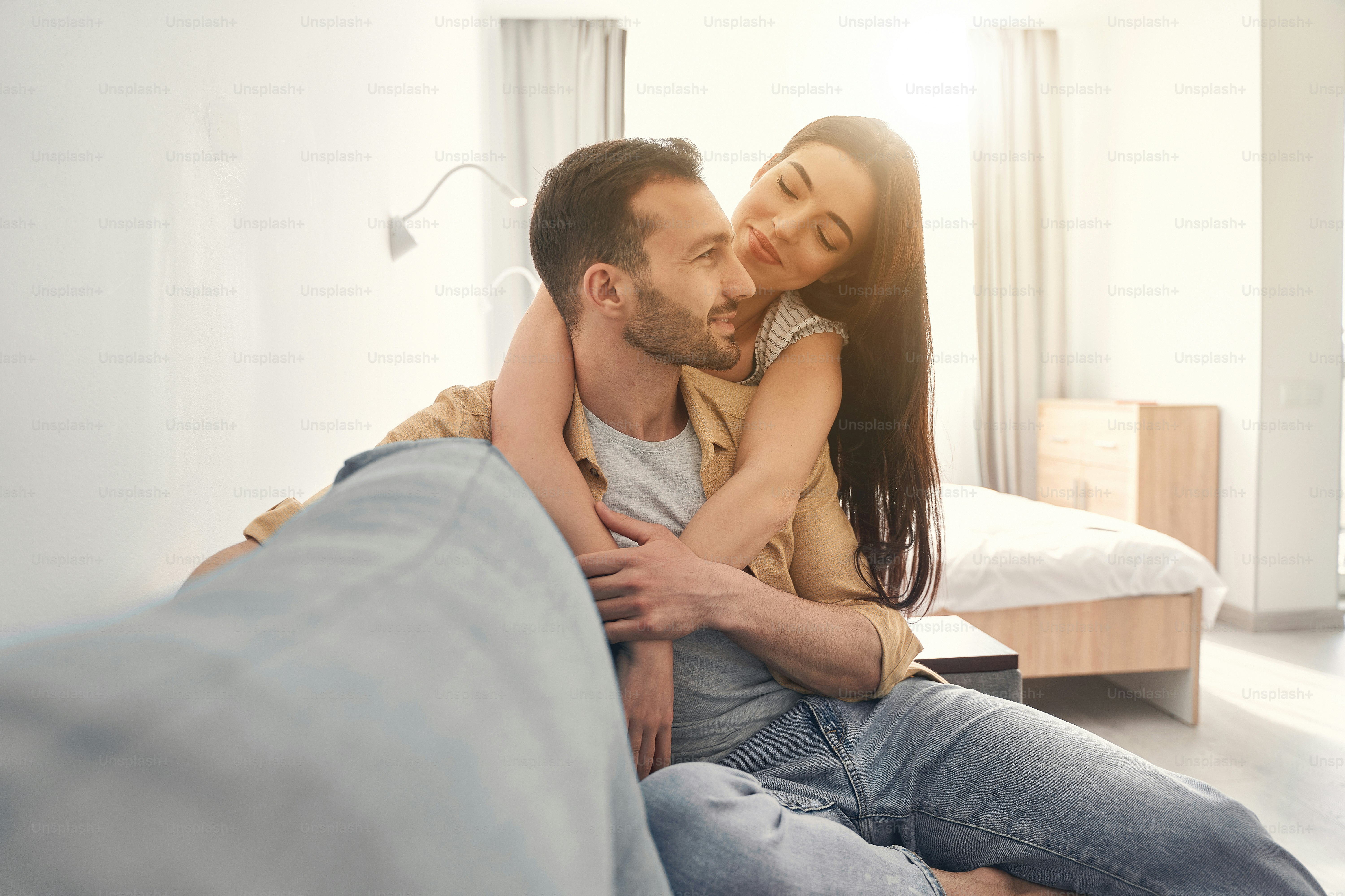 Smiling man and woman in love spending free time together and sitting at home on a cosy sofa, hugging