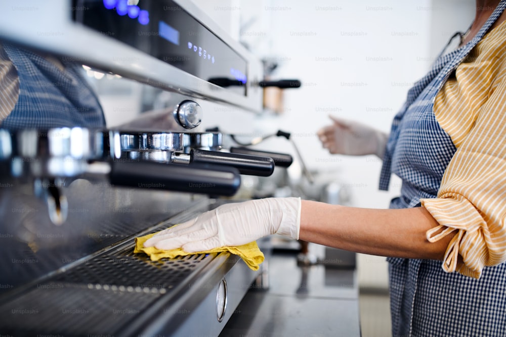 Coffee shop woman owner working with gloves, cleaning and disinfecting machine.