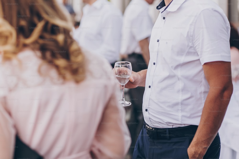 Man holding champagne glass, toasting at wedding reception or corporate party outdoors. Toast for new happy wedding couple. Guests cheering with glasses