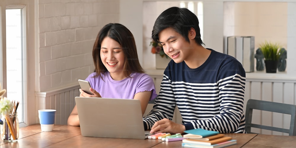 Young couple working with computer laptop and tablet while sitting together at the wooden working desk over comfortable sitting room as background.