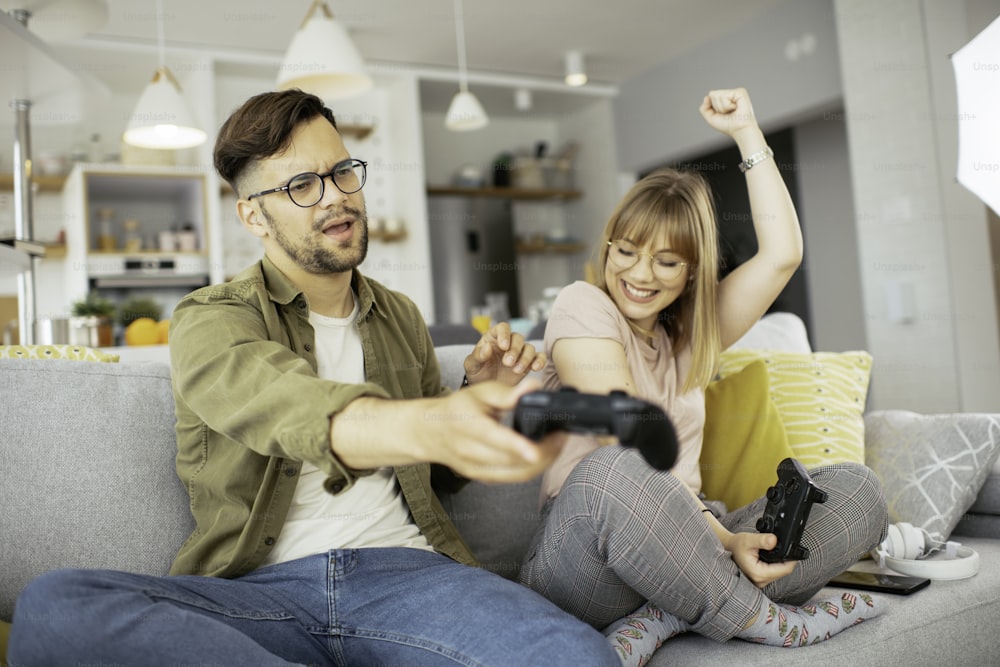 Boyfriend and girlfriend playing video game with joysticks in living room.
Loving couple are playing video games at home.