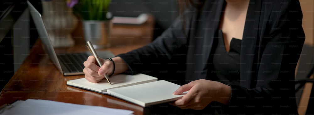 Cropped shot of businesswoman taking note on notebook on wooden worktable with laptop and document file