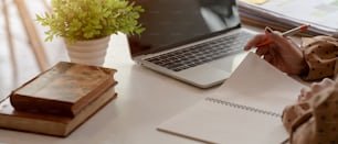 Cropped shot of female entrepreneur reading information on notebook while working at simple workspace with laptop, books and decoration