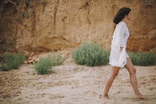 Carefree boho girl in white summer dress walking on beach. Happy young woman relaxing on seashore. Summer vacation. Mindfulness and relaxation. Lifestyle