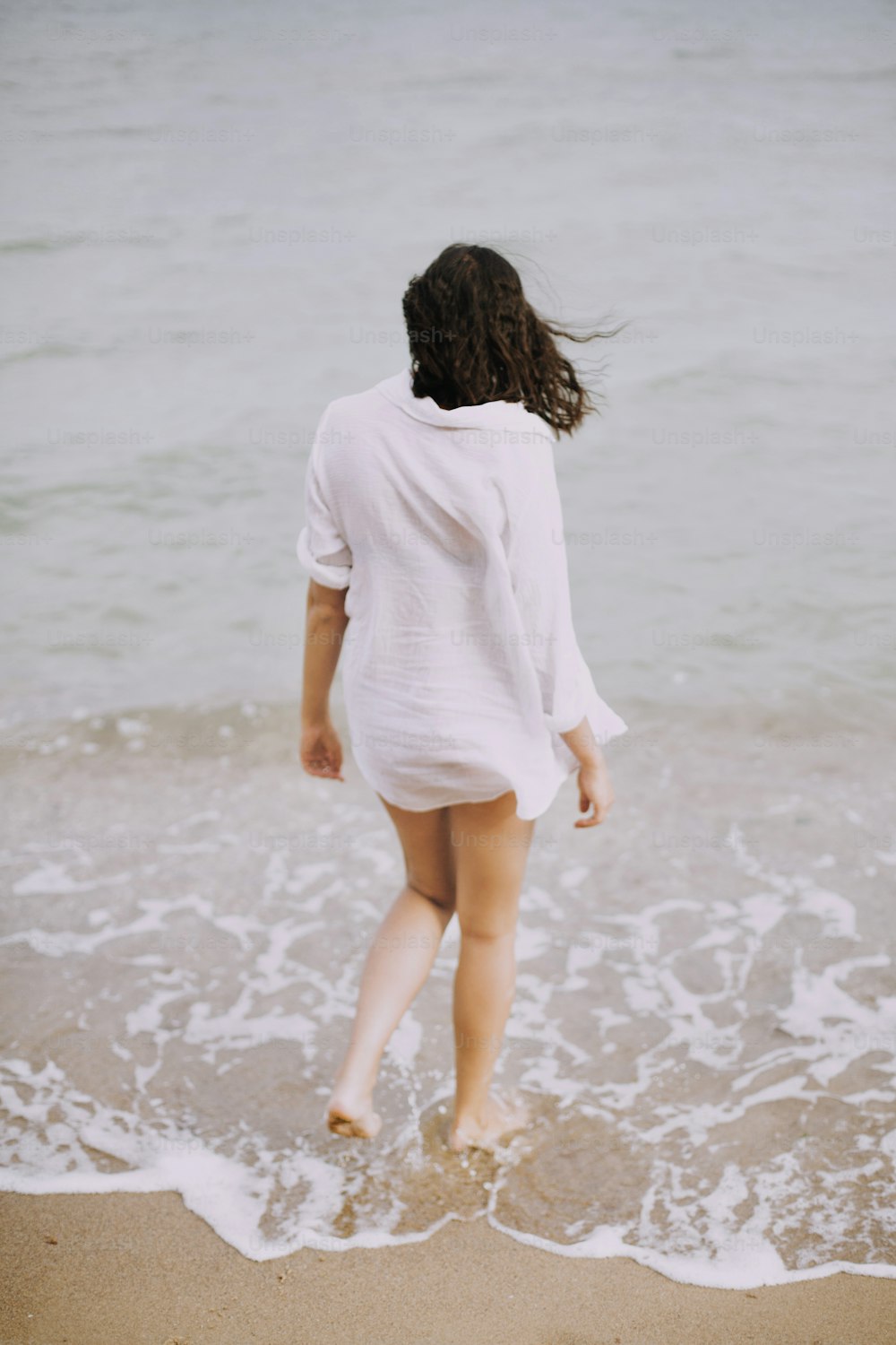 흰 셔츠를 입은 보헤미안 소녀가 바다 파도에 해변을 걷고 있다. 해변에서 휴식을 취하는 행복한 젊은 여성. 여름 방학. 마음 챙김과 휴식. 생활방식