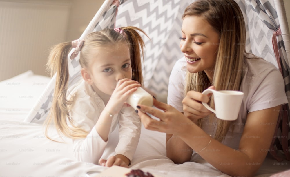 Milk is good for your growth. Mother and daughter having breakfast in bed.