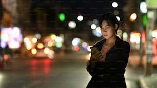 Asian woman requesting a ride with a smartphone in downtown city street at night