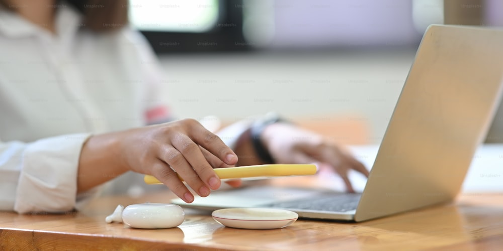 Imagen recortada de una mujer de oficina está cargando un teléfono inteligente con un cargador inalámbrico mientras escribe en una computadora portátil.