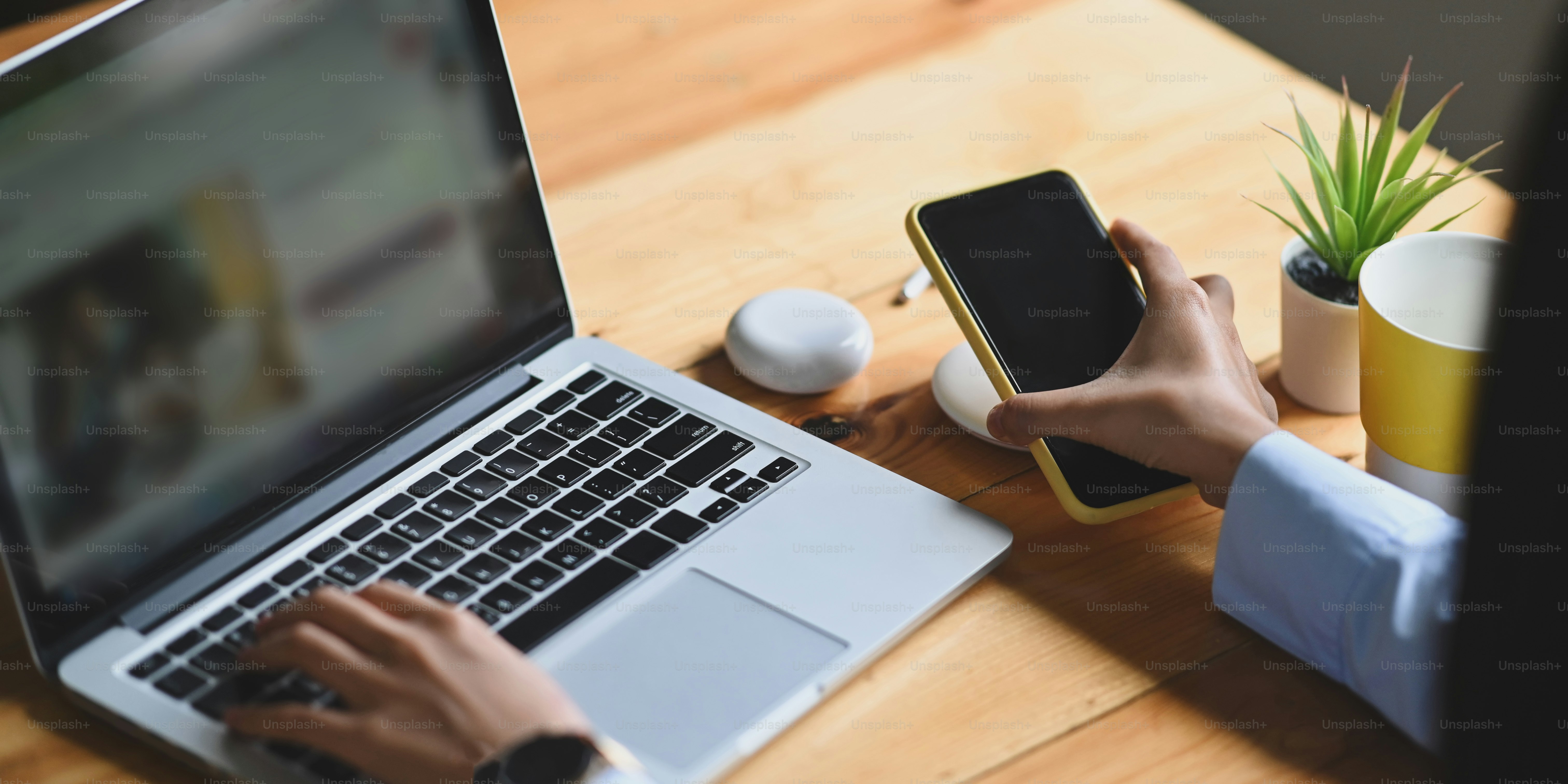 Cropped image of an office woman is charging a smartphone with a wireless charger while typing on a computer laptop.