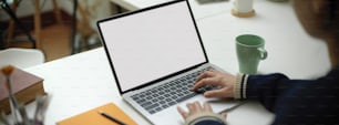 Close up view of female employee working on mock-up laptop with mug and stationery on portable workspace