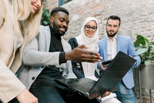 다민족의 다양한 사업가, 두 남자와 두 여자로 구성된 팀이 현대 사무실에 서서 노트북과 태블릿을 사용하여 토론하고 함께 작업합니다. 비즈니스 및 디지털 기술.